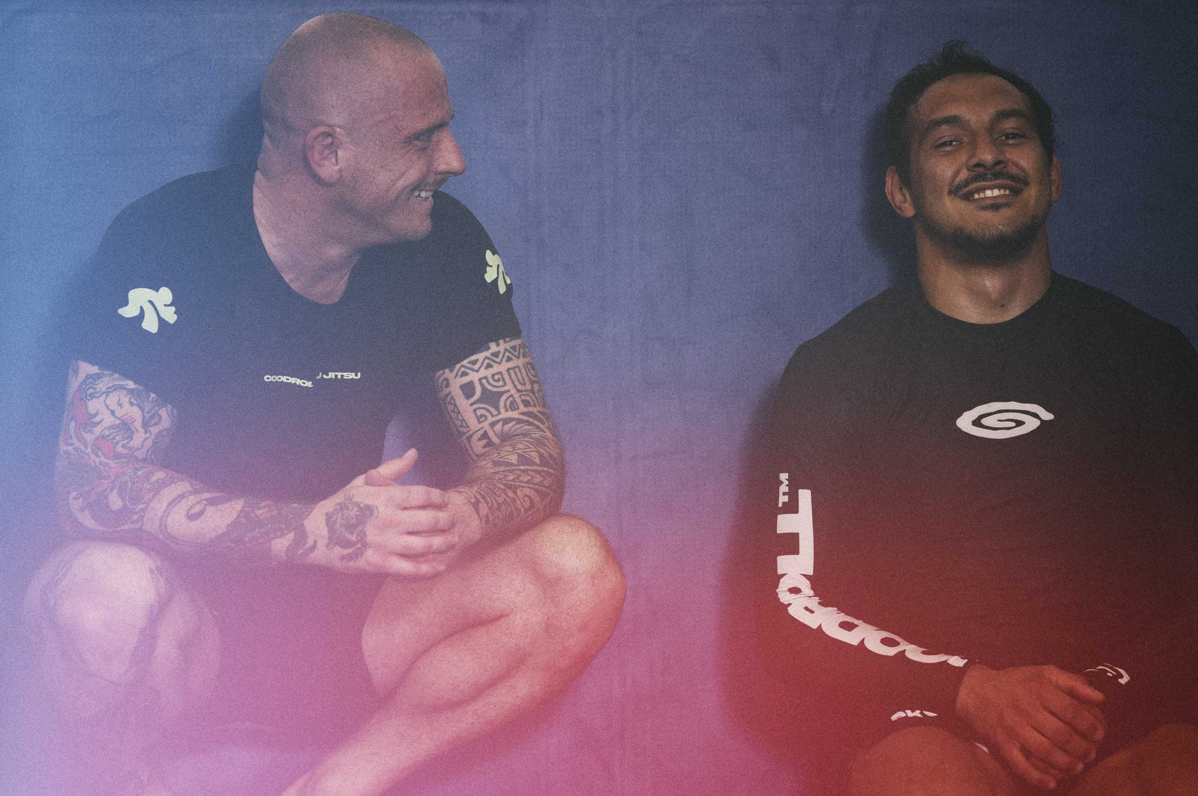 Two people sitting on a gym mat and laughing. Both are wearing the Goodroll Jiu-Jitsu rashguard.