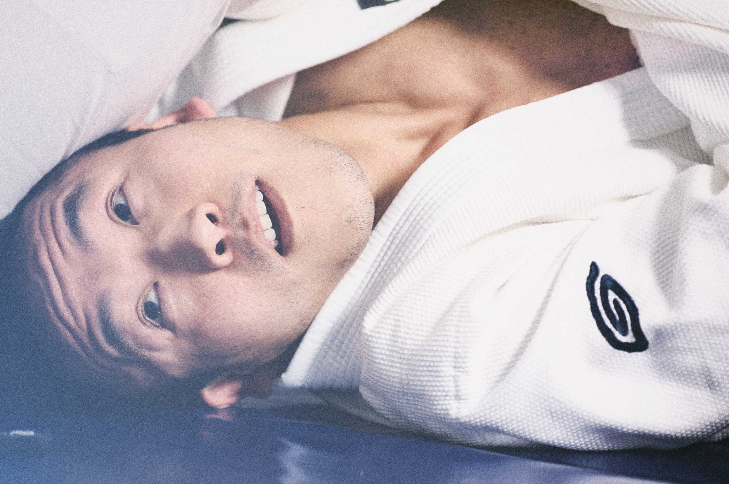 A person lying on a gym mat. He is wearing the Goodroll Brazilian Jiu-Jitsu Heritage gi.