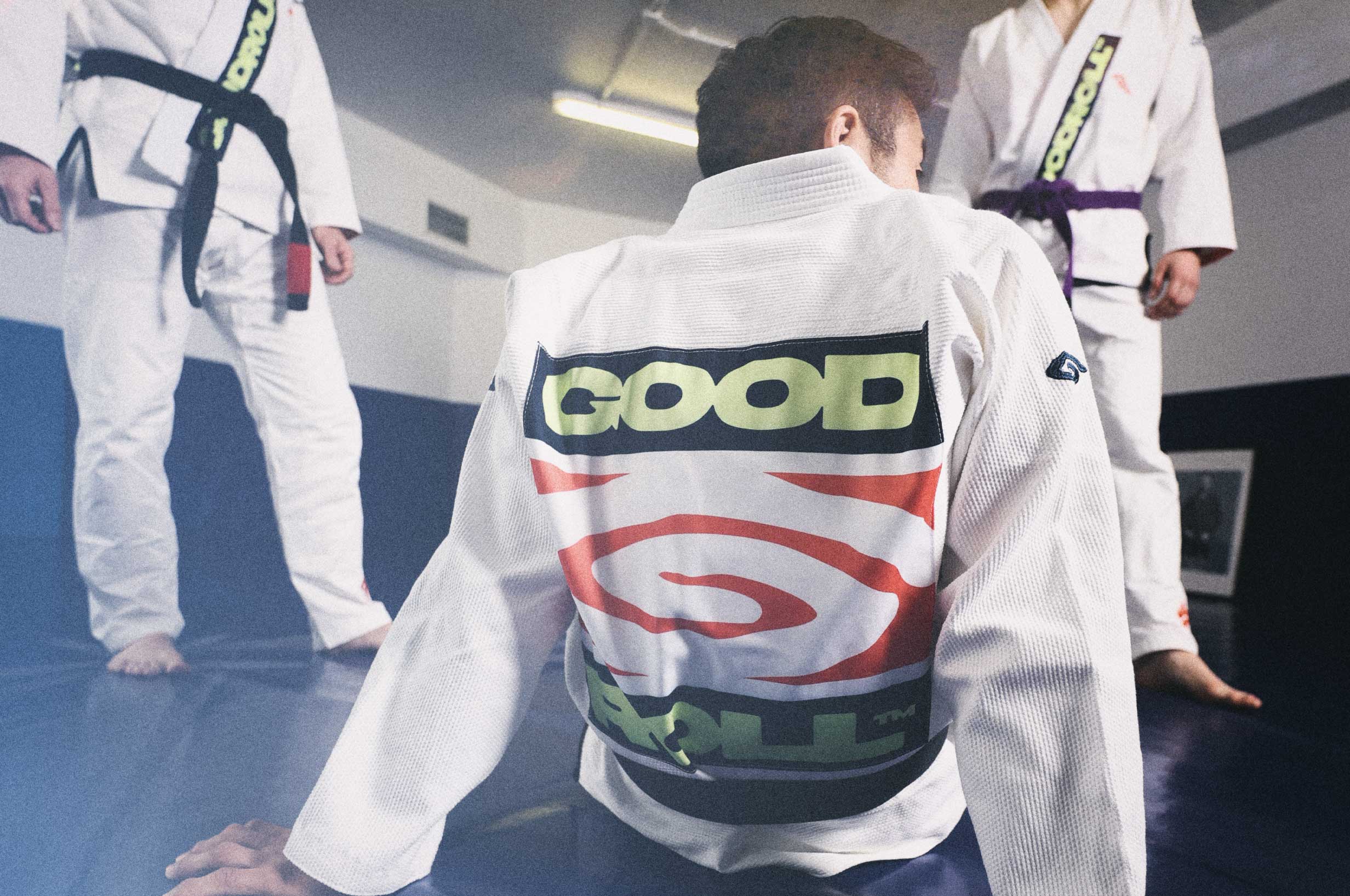 Three people on a gym mat, each wearing a Goodroll Brazilian Jiu-Jitsu Heritage Gi